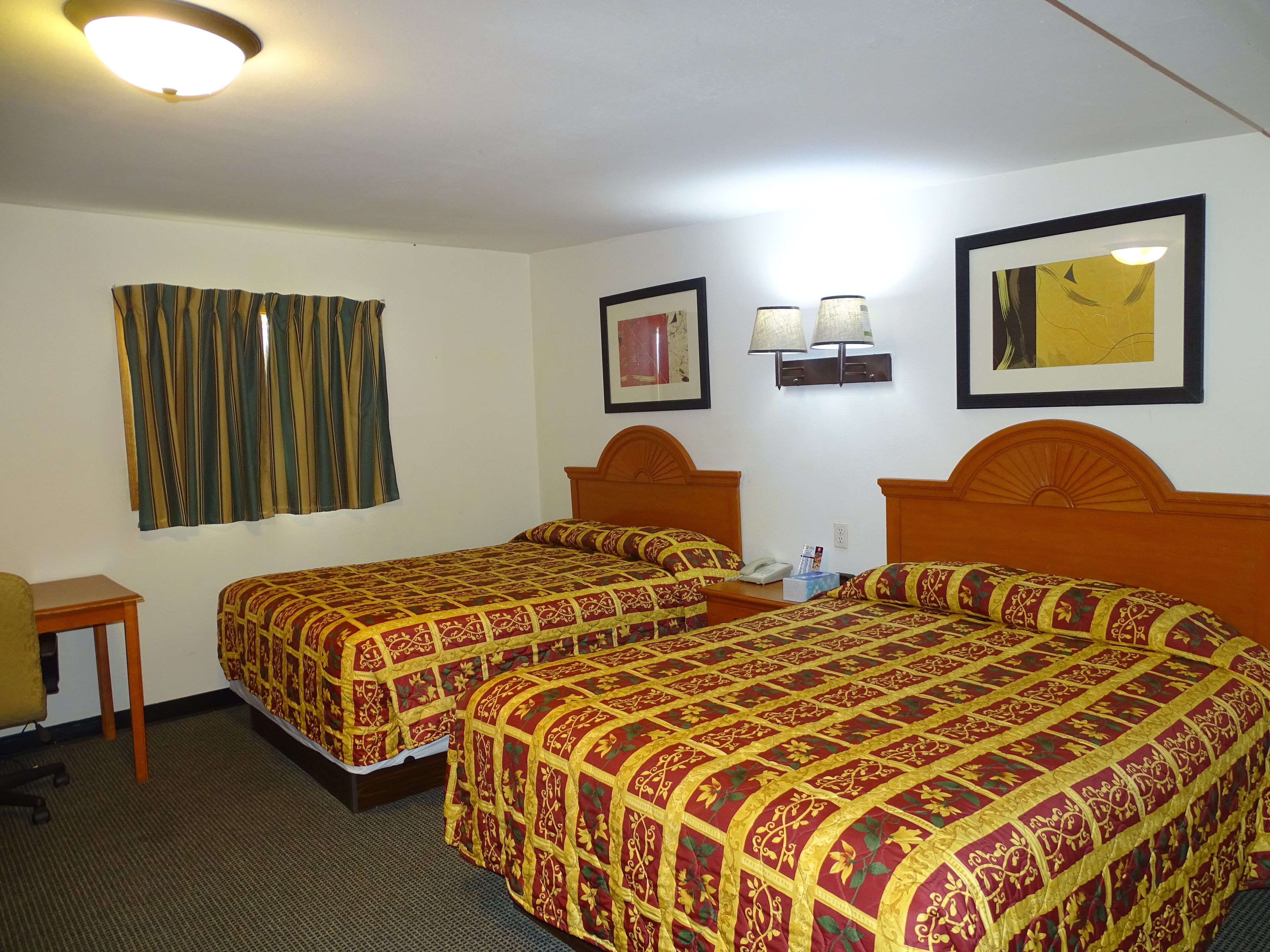 A hotel room with two beds, a desk, a chair, and two wall-mounted lamps.