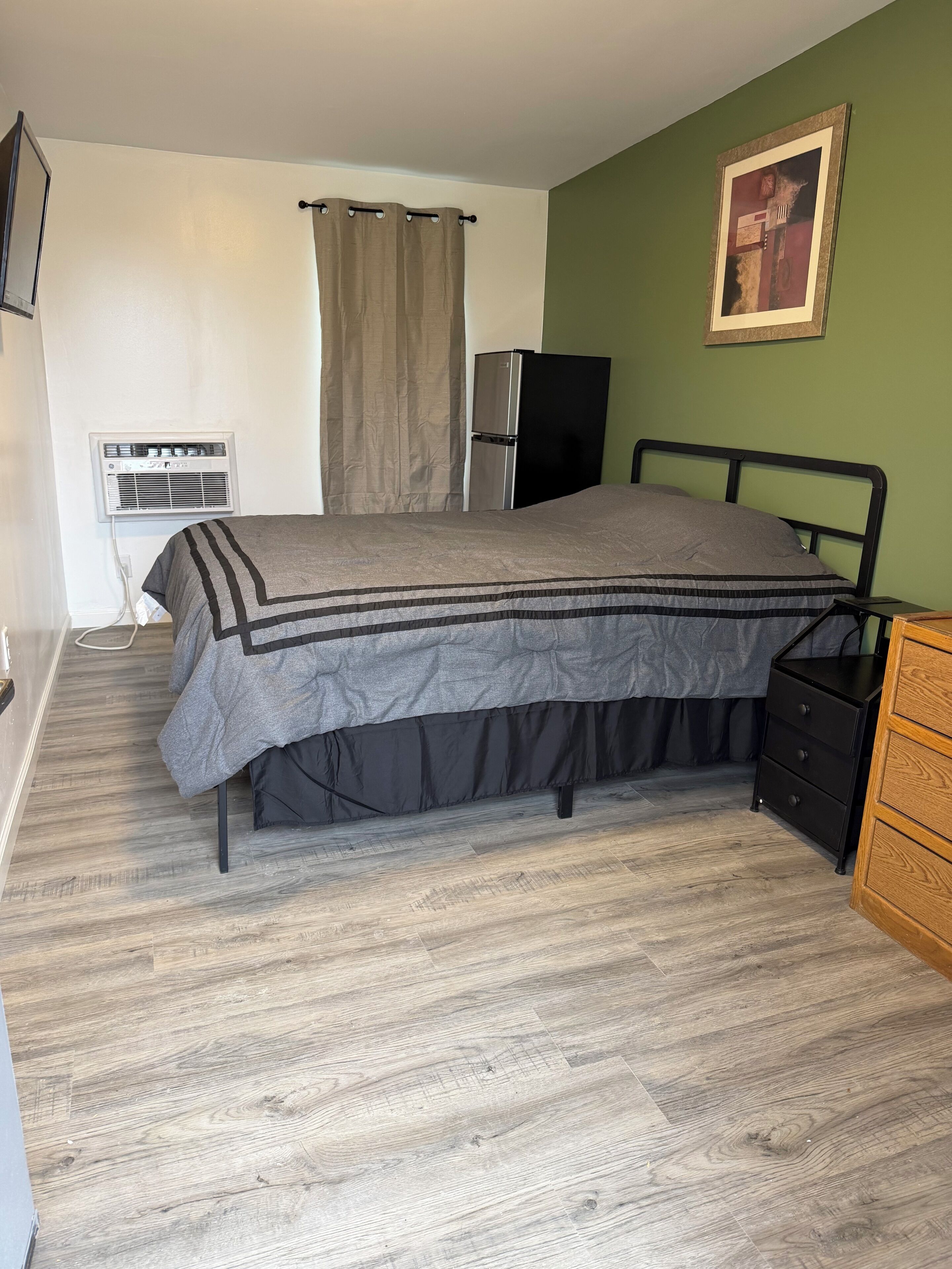A bedroom with a bed, a dresser, a wall-mounted air conditioner, and a painting.