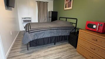 A bedroom with a bed, a dresser, a TV, an air conditioner, and a microwave.
