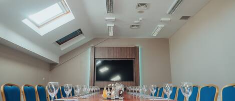 A conference room with a long table, blue chairs, a flat-screen TV, and skylights.