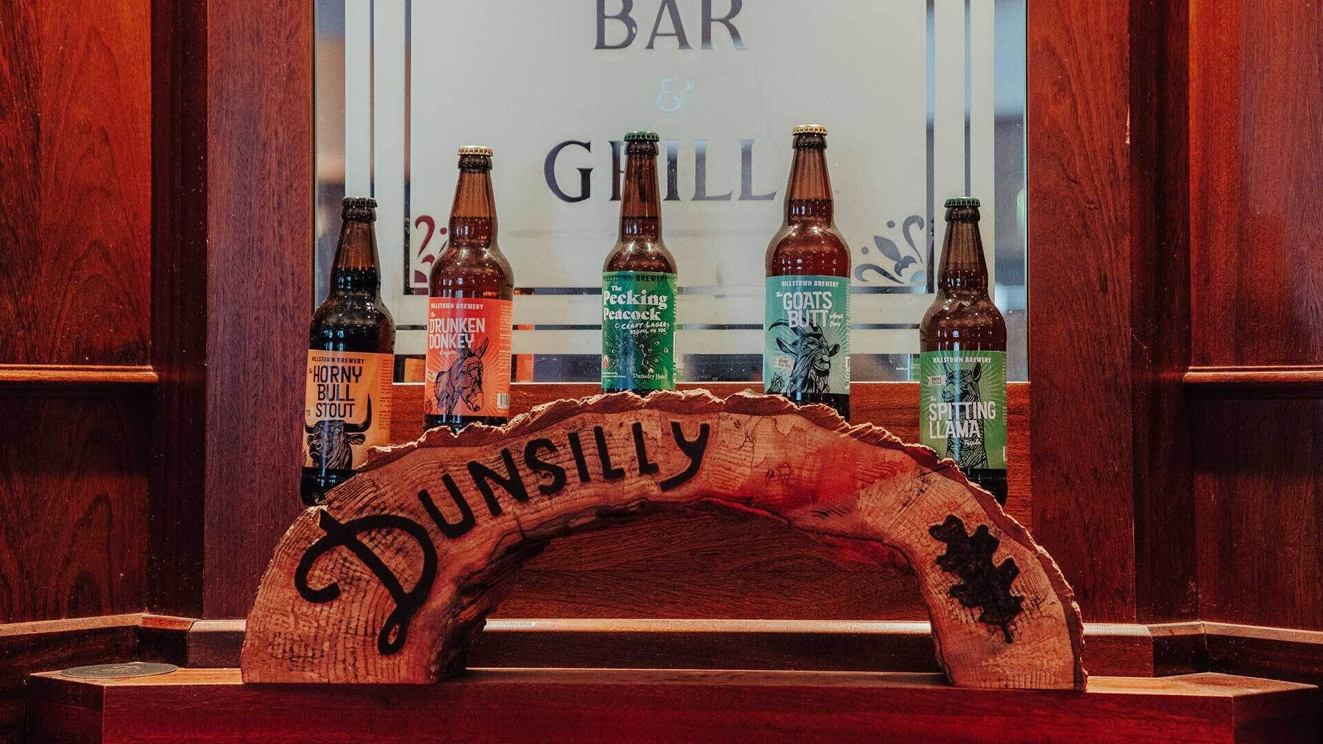 A wooden sign with the name "DUNSILLY" above a selection of beer bottles.