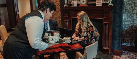 A man and a woman sitting at a table with a laptop, two cups of coffee, and a menu.