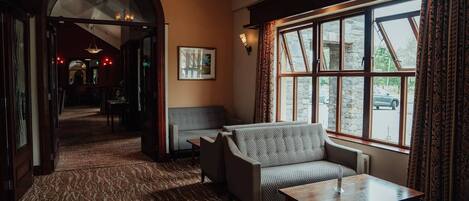 A cozy room with a patterned carpet, a sofa, a table, and a large window with curtains.