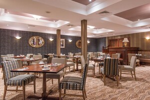 Un comedor de hotel con varias mesas y sillas, espejos grandes y un piano.