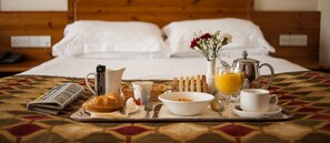 A neatly arranged breakfast tray on a bed with a quilt, a newspaper, a croissant, a bowl of cereal, a jug of orange juice, a cup of coffee, and a vase of flowers. - Dunsilly Hotel (Antrim)