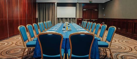 A conference room with a long table, blue chairs, and a projector screen.