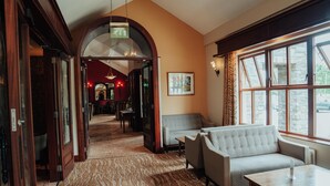 Una hall d'albergo con tappeto a motivi, una poltrona, un tavolino e un'ampia finestra con cornice in pietra.