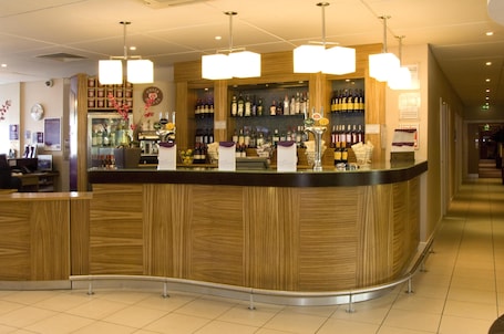 A bar area with wooden counter, hanging lights, and shelves of bottles.