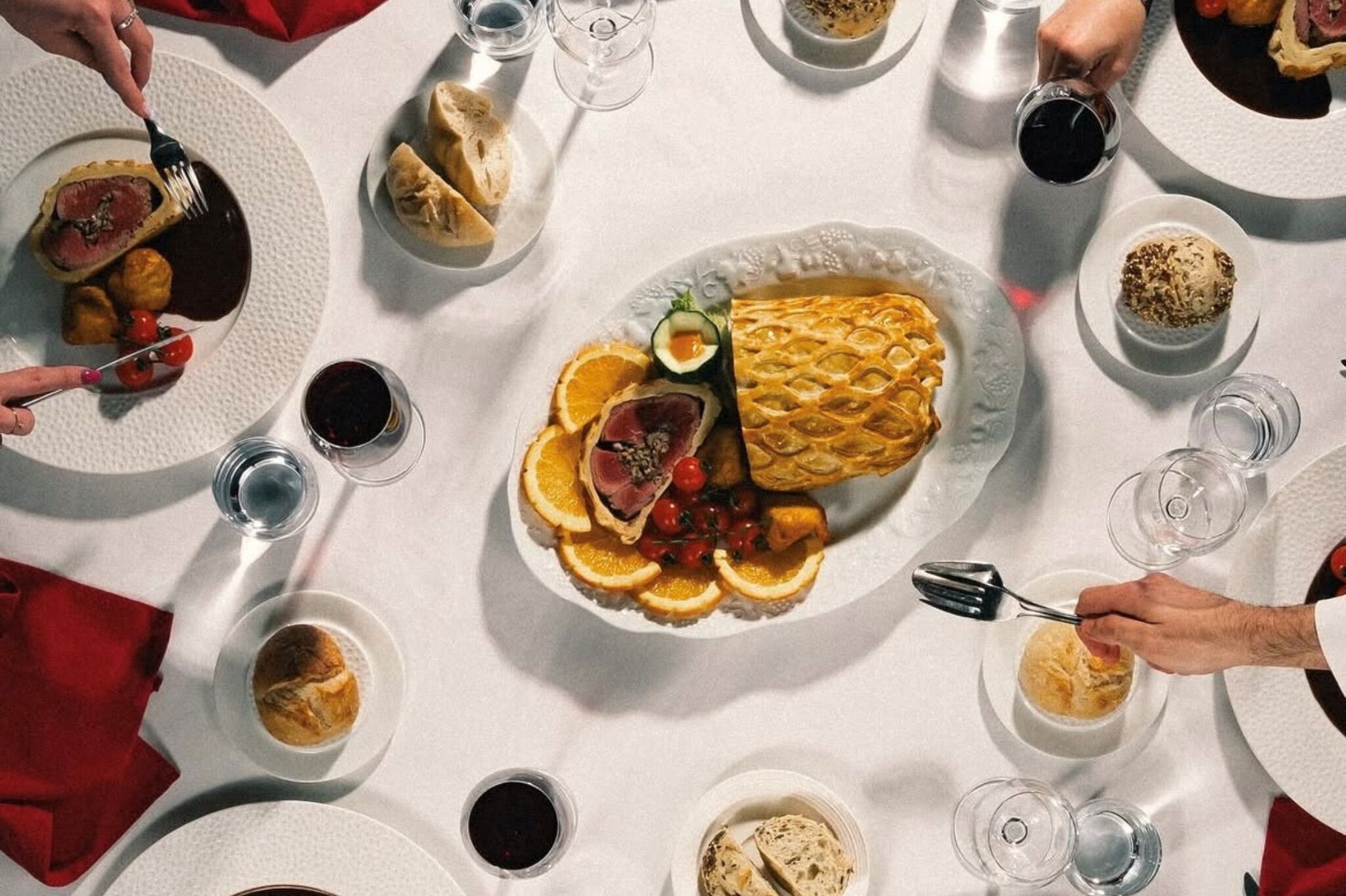 A round dining table with various dishes, including a waffle, meat, and vegetables, surrounded by glasses of water and wine.