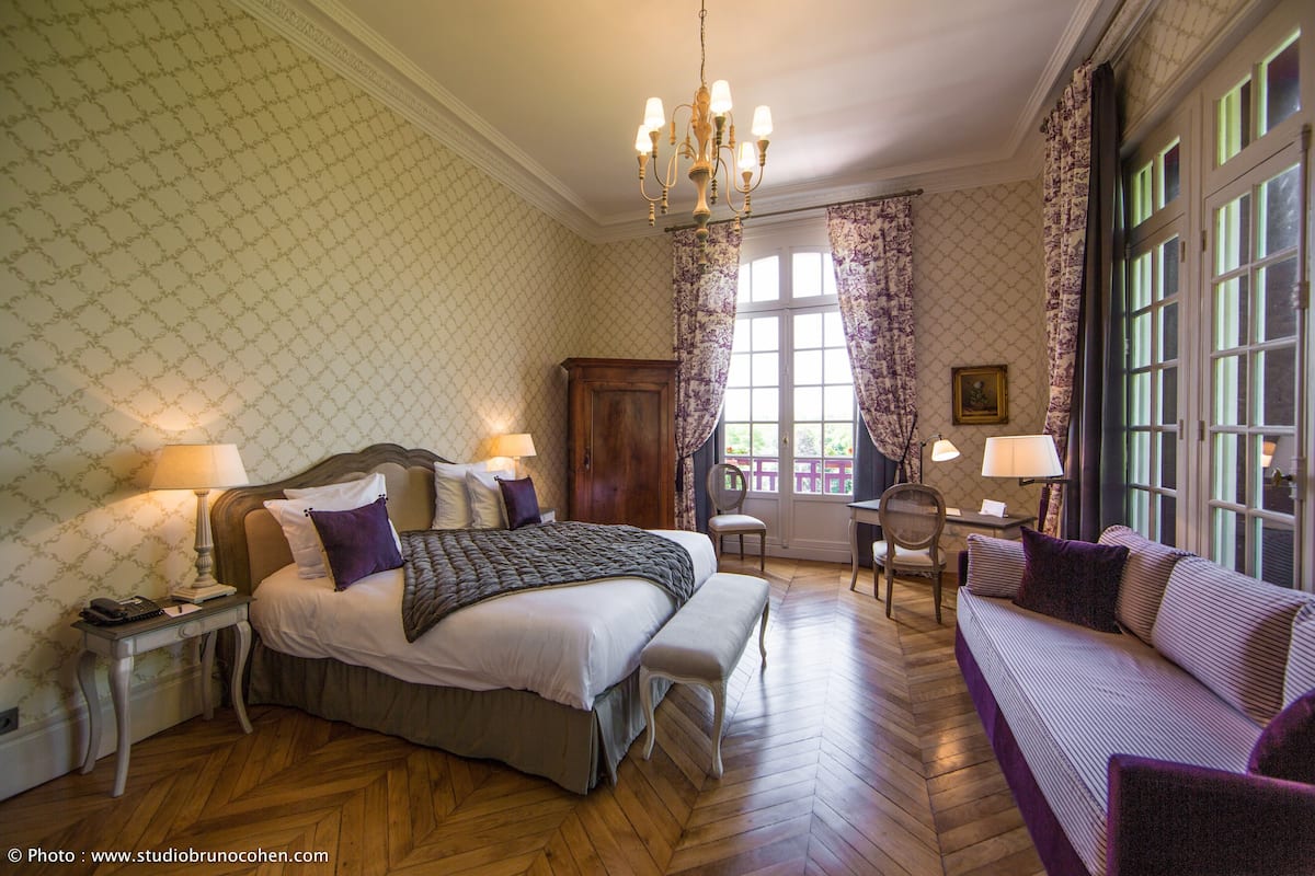Een slaapkamer met een groot bed, een zithoek met een bank, een houten nachtkastje en een bureau met stoel.