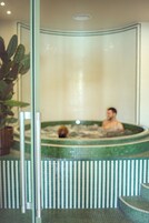 Una persona en un jacuzzi con una pared de azulejos y una planta en maceta.