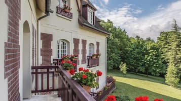 A two-story house with a balcony, red flowers, and a well-maintained lawn.