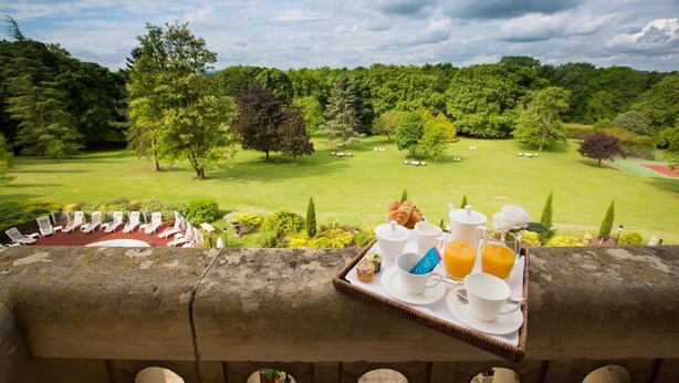Un plateau de petit-déjeuner avec des croissants, du café et du jus d’orange, posé sur un balcon donnant sur un terrain de golf.