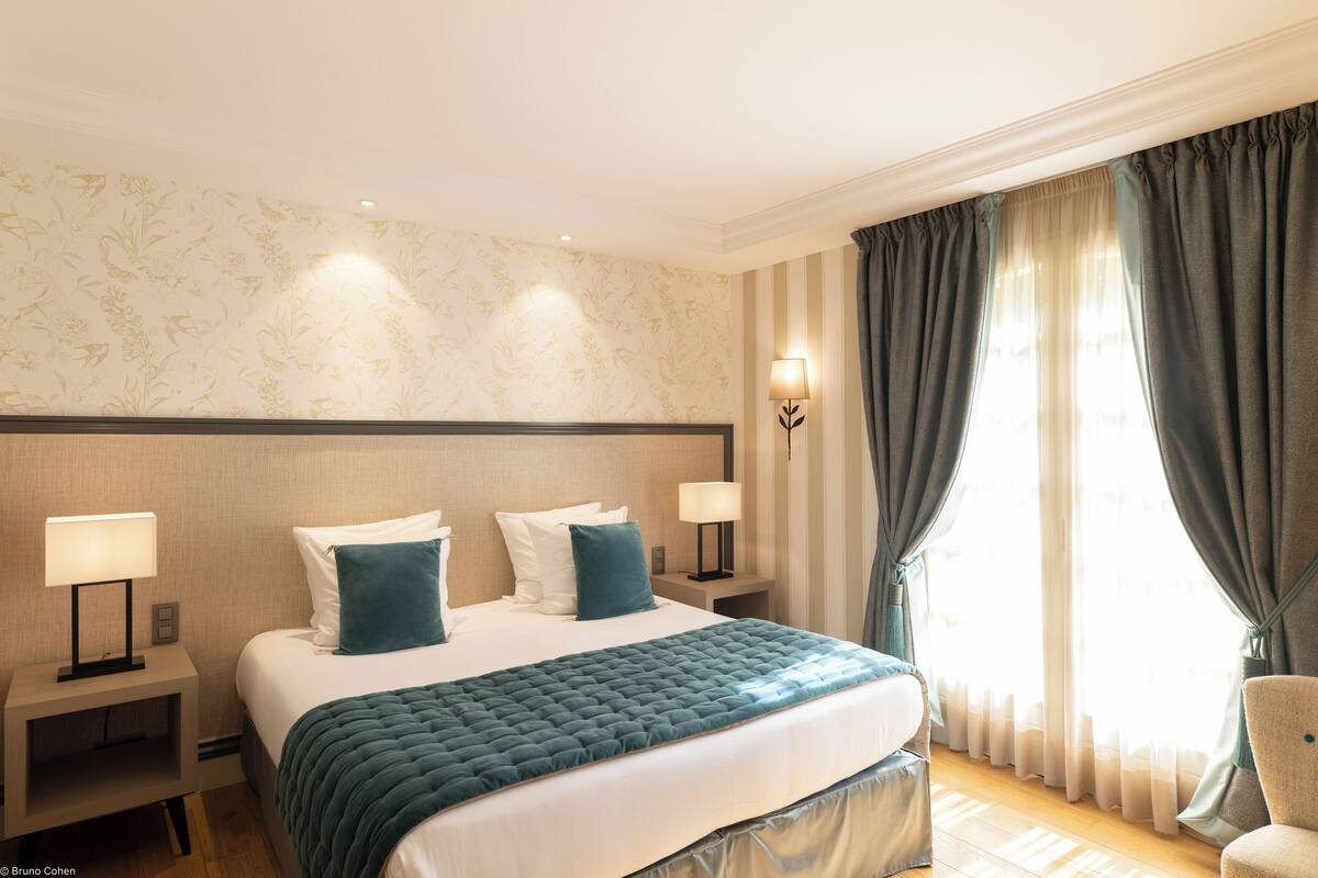 Een hotelkamer met een groot bed, twee nachtkastjes, een lamp en een raam met gordijnen.