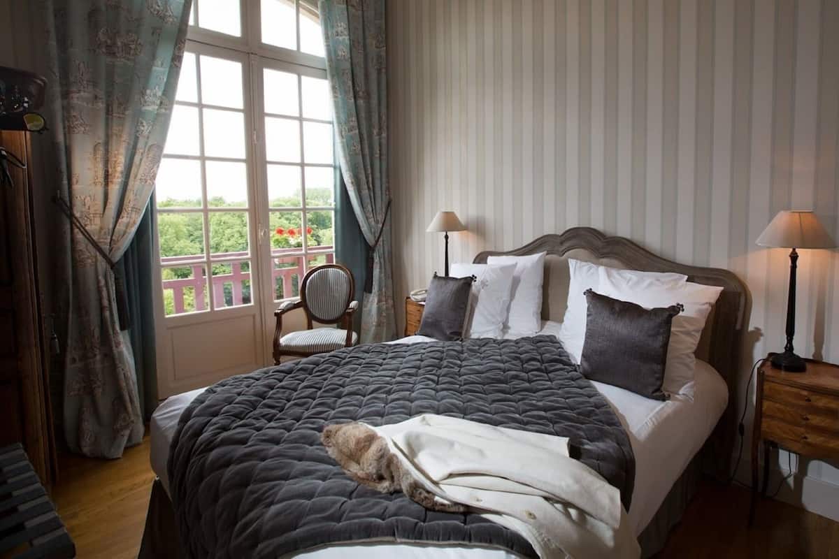 Een slaapkamer met een groot bed, twee nachtkastjes, een stoel en een raam met gordijnen.
