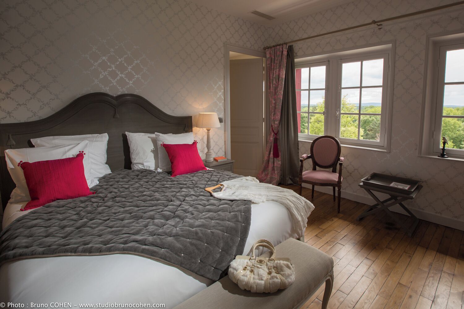 A bedroom with a large bed, a chair, a small table, and a window with a view.