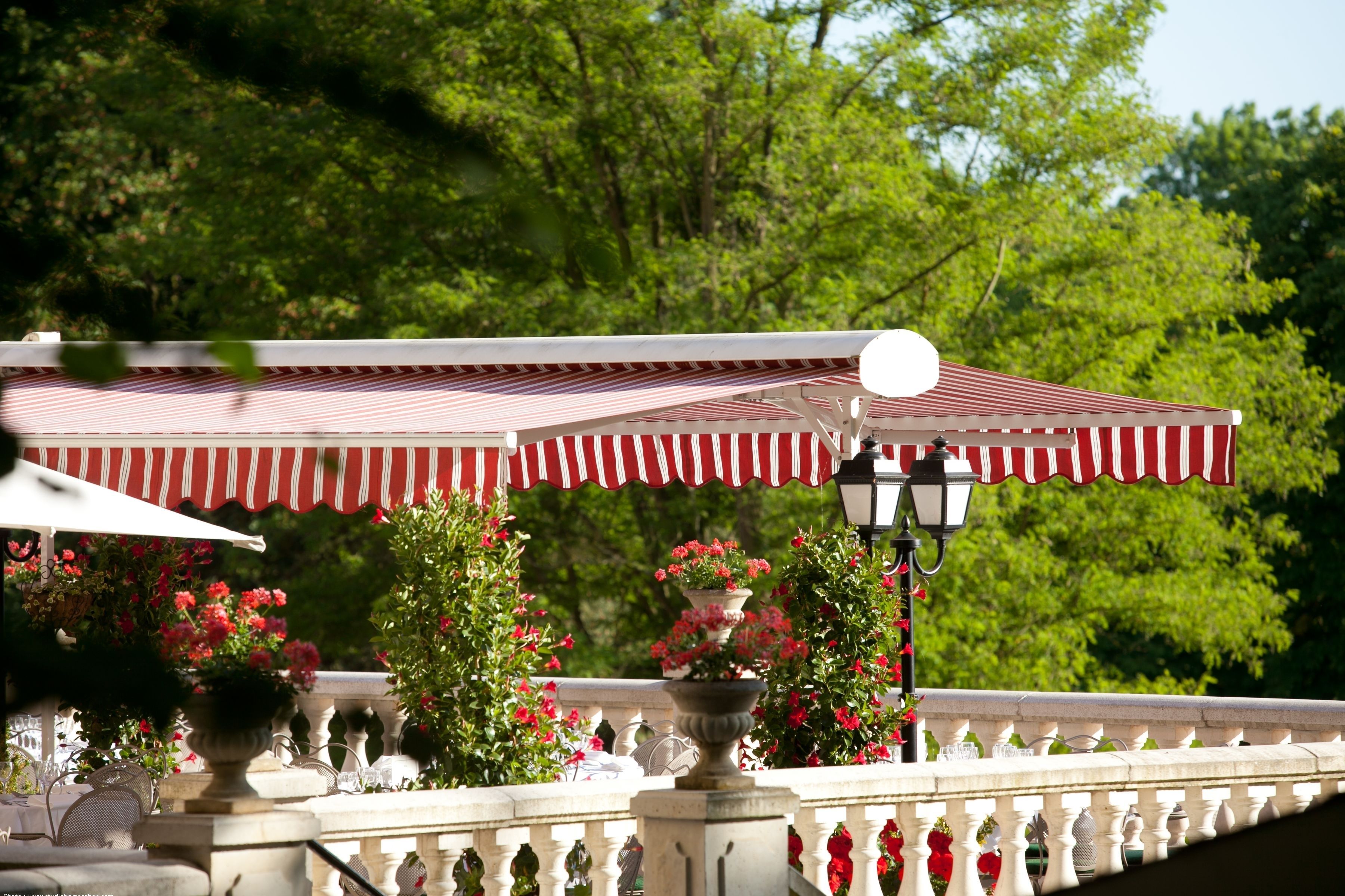 A balcony with a red and white striped awning, potted plants, and a white balustrade.