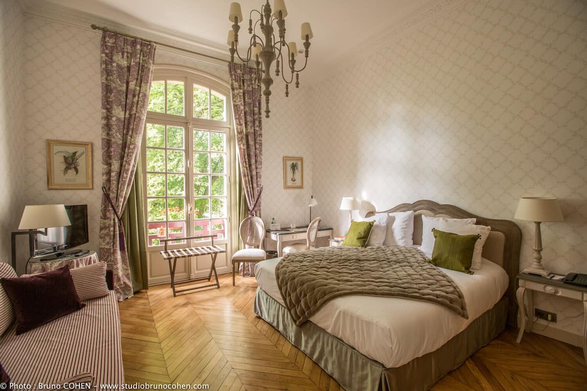 Een goed verlichte slaapkamer met een groot bed, een bureau, een stoel en een televisie.