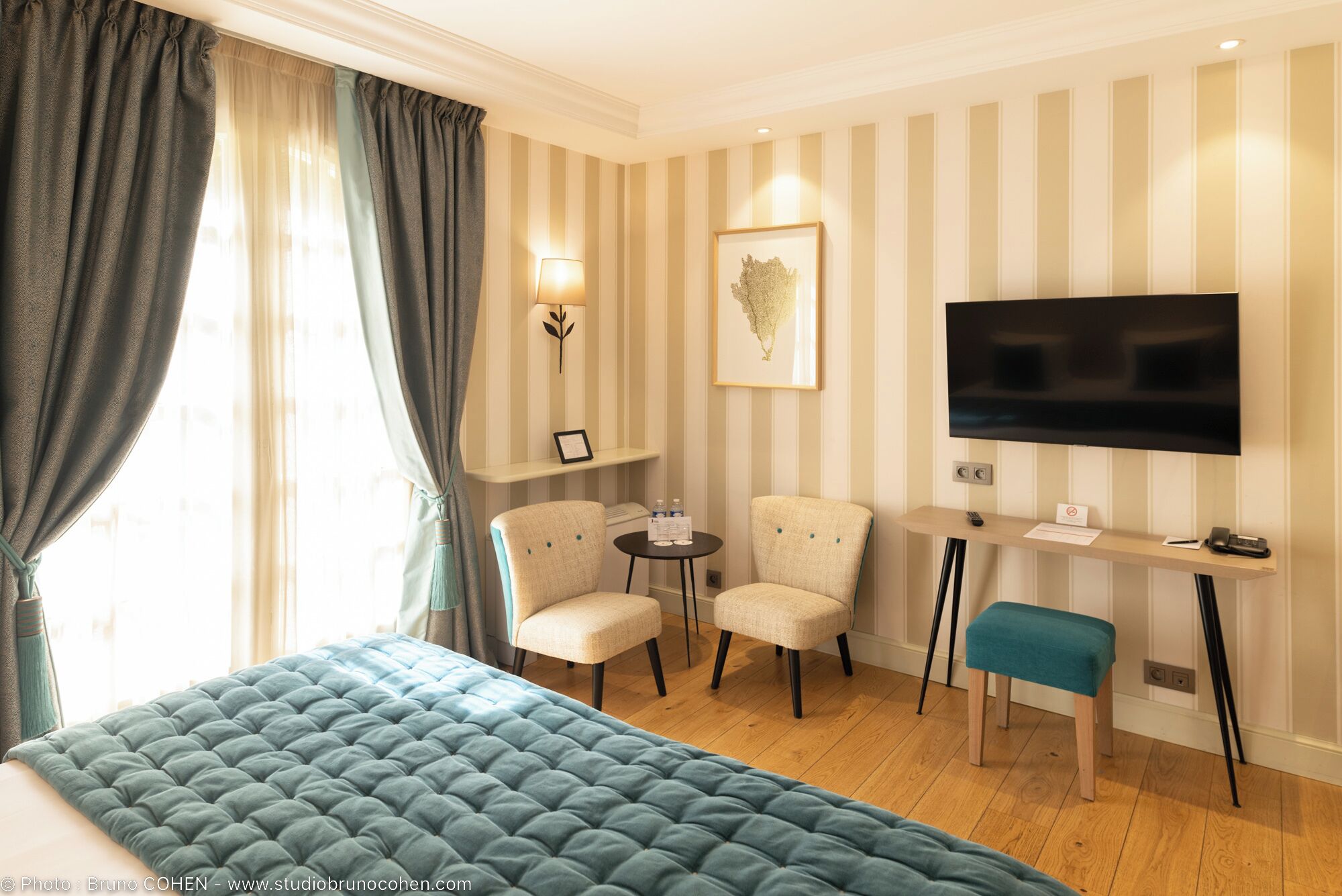 A hotel room with a large bed, a desk with a TV, two chairs, and a small table.