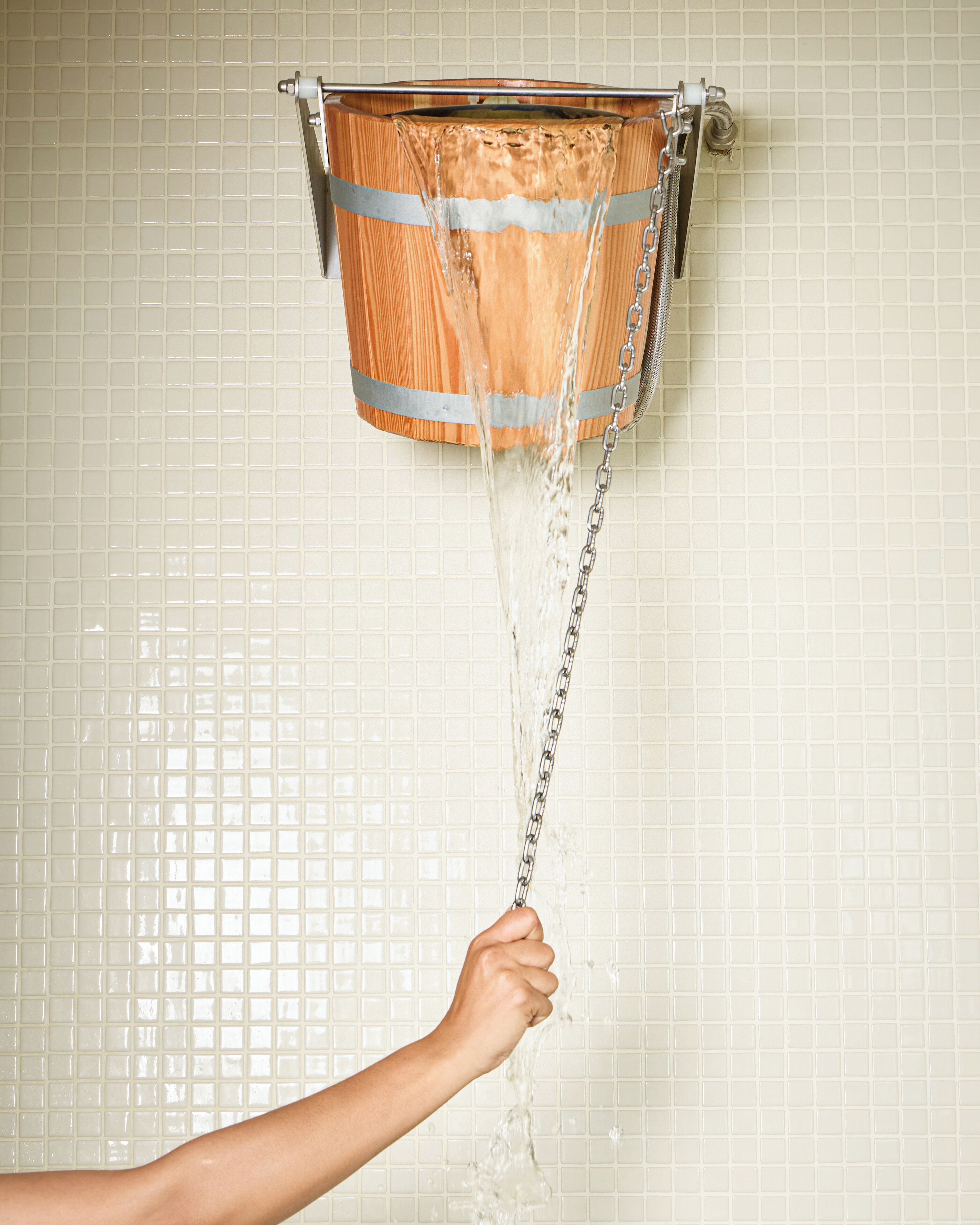 A hand holding a chain attached to a wooden bucket with water flowing through it.
