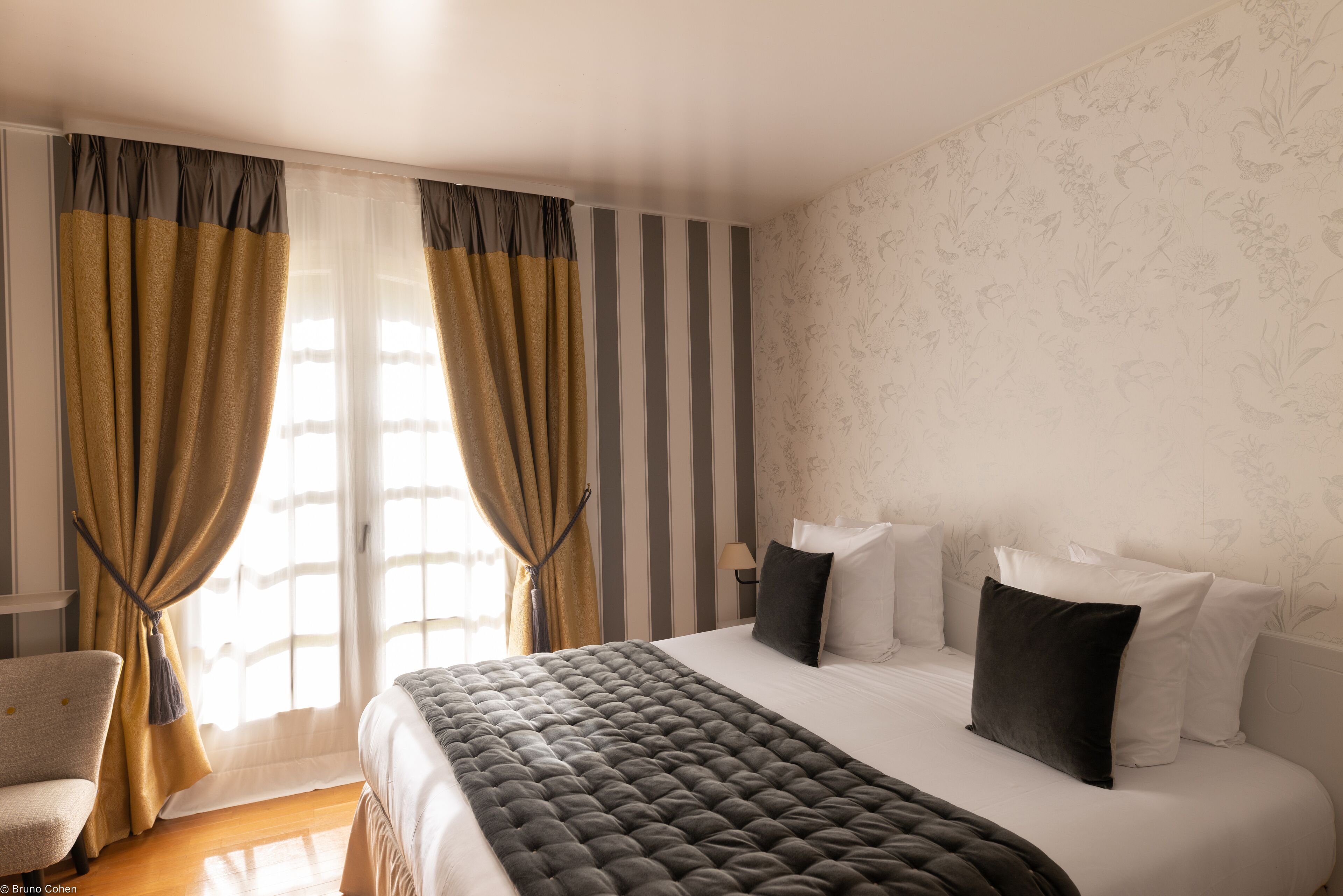 Una habitación de hotel con una cama grande, una silla y un ventanal con cortinas.