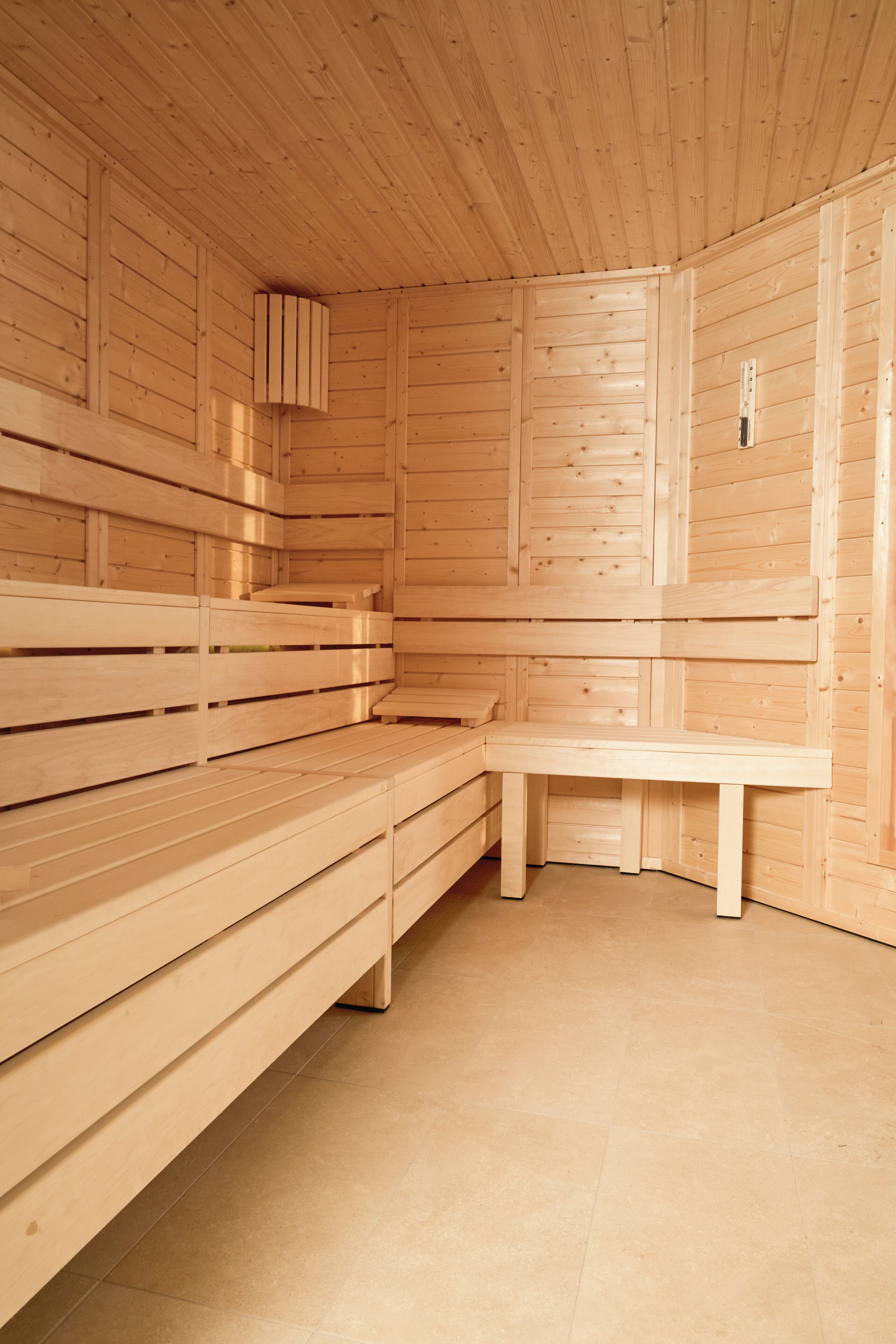 A wooden sauna with benches and a bench seat, featuring a sloped ceiling and wooden walls.