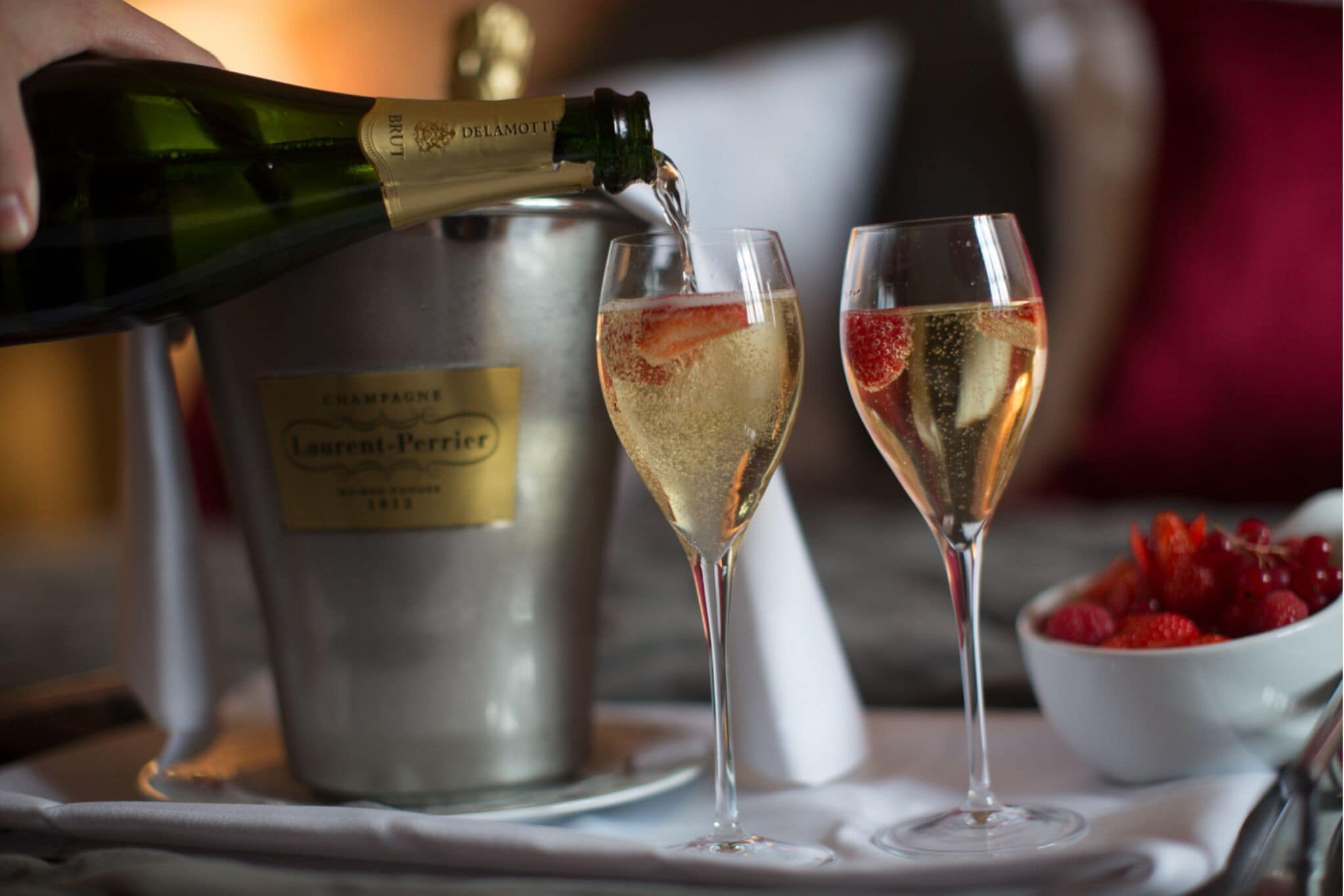 Una bottiglia di champagne viene versata in due bicchieri, con un secchio recante l'etichetta "Champagne Laurent Perrier" sullo sfondo.