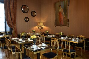 A dining area with tables set for service, chairs, a lamp, and a painting on the wall. - Chateau Colbert (Maulevrier)