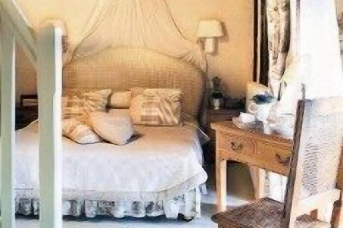 A bedroom with a canopy bed, a nightstand, a lamp, and a chair.