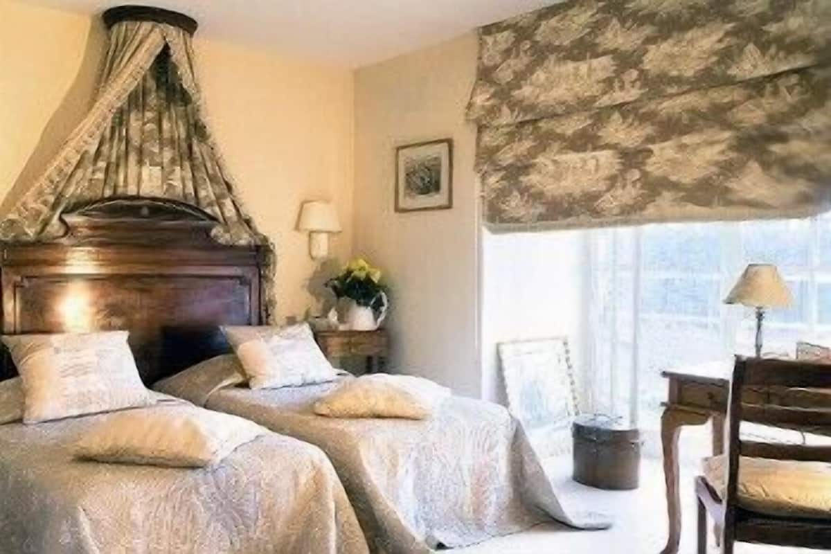 A bedroom with two beds, a wooden headboard, a window with a view, and a chair.