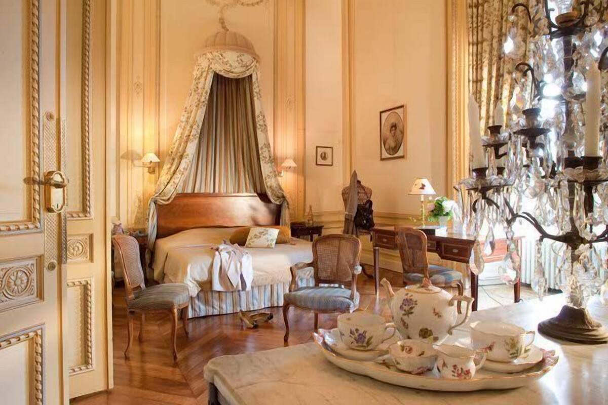 A classic hotel room with a four-poster bed, a chandelier, and a tea set on the side table.