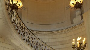 A grand staircase with ornate metal railings and a chandelier, leading to a reception area with a decorative floor pattern and a sign reading "Chateau Collection." - Chateau Colbert (Maulevrier)