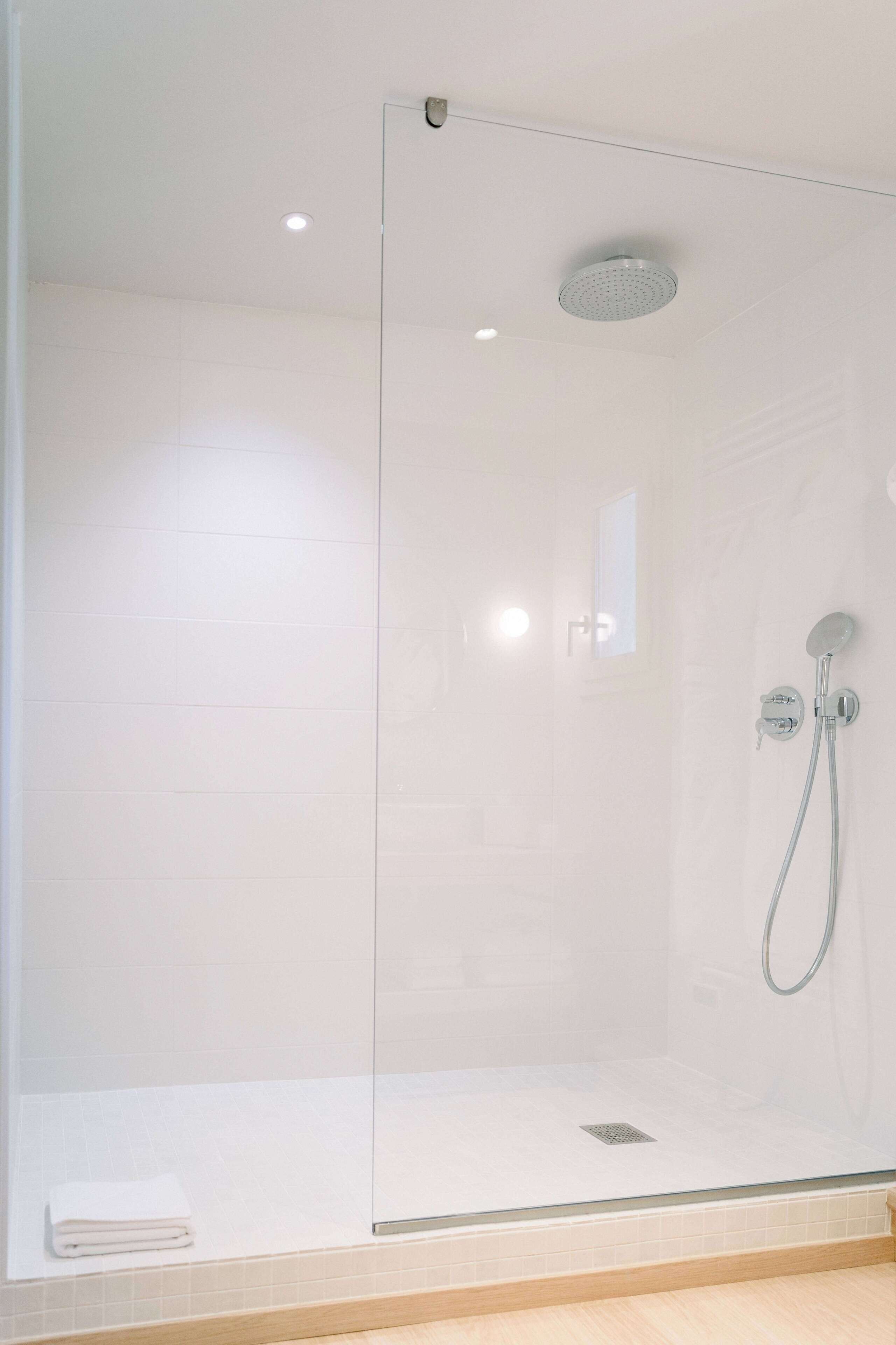 A glass-enclosed shower with a handheld showerhead and a wall-mounted faucet.