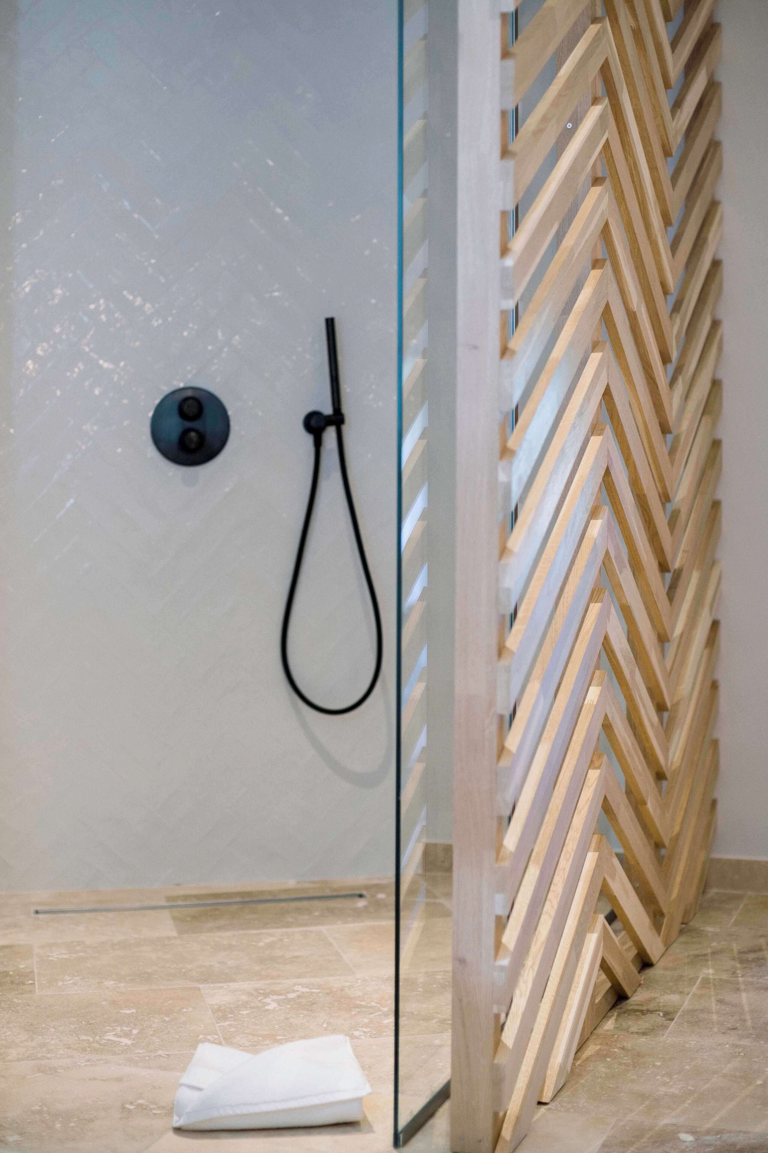 Un espace douche avec un mur en bois disposé en motif de chevron, une paroi en verre et une serviette blanche sur le sol.