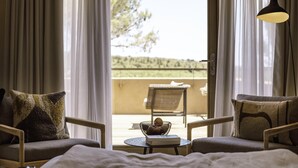Ein Zimmer mit zwei Sesseln, einem kleinen Tisch und Blick auf einen Außenbereich mit Stuhl und Tisch.