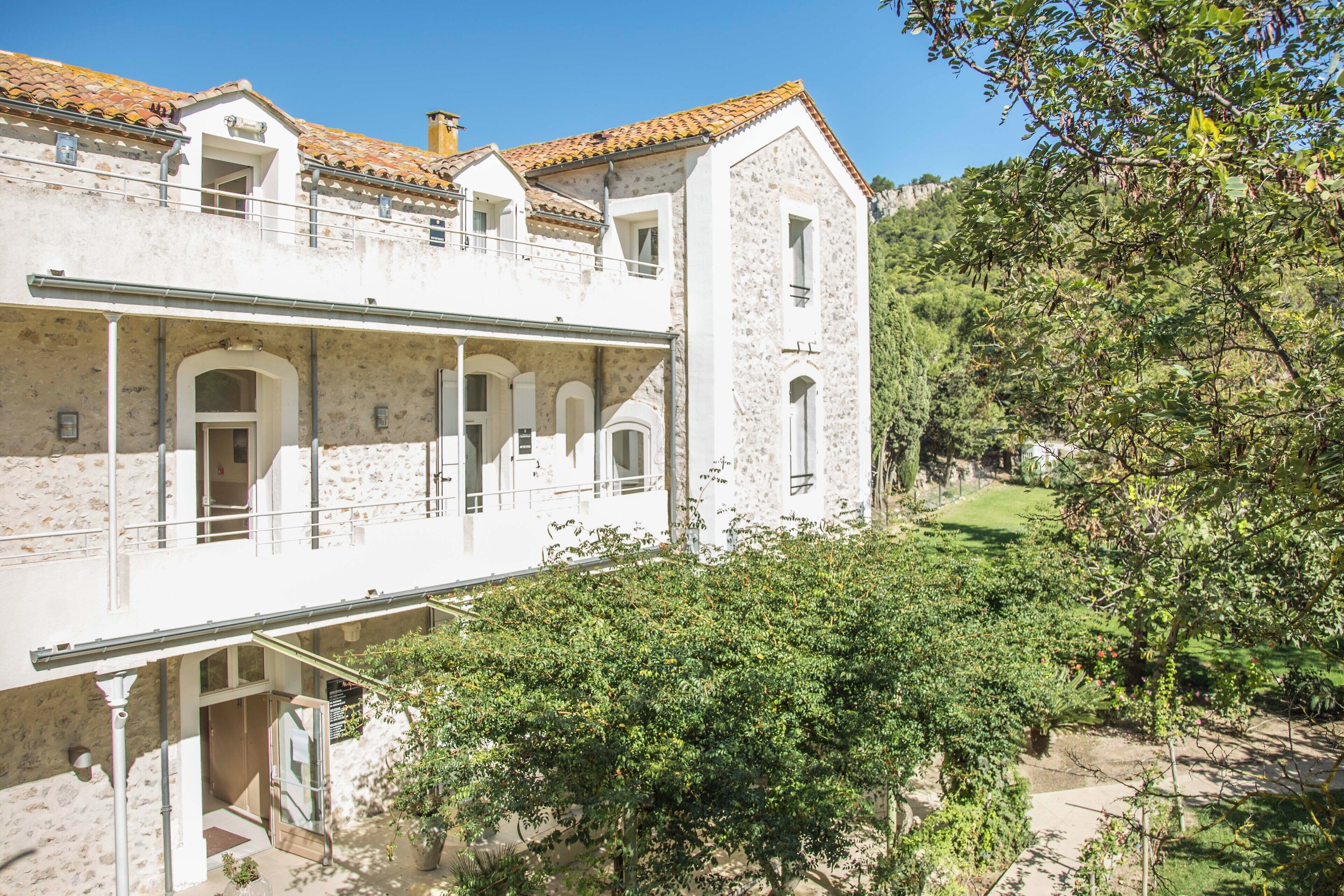 A two-story building with a stone facade, a balcony, and a garden area.