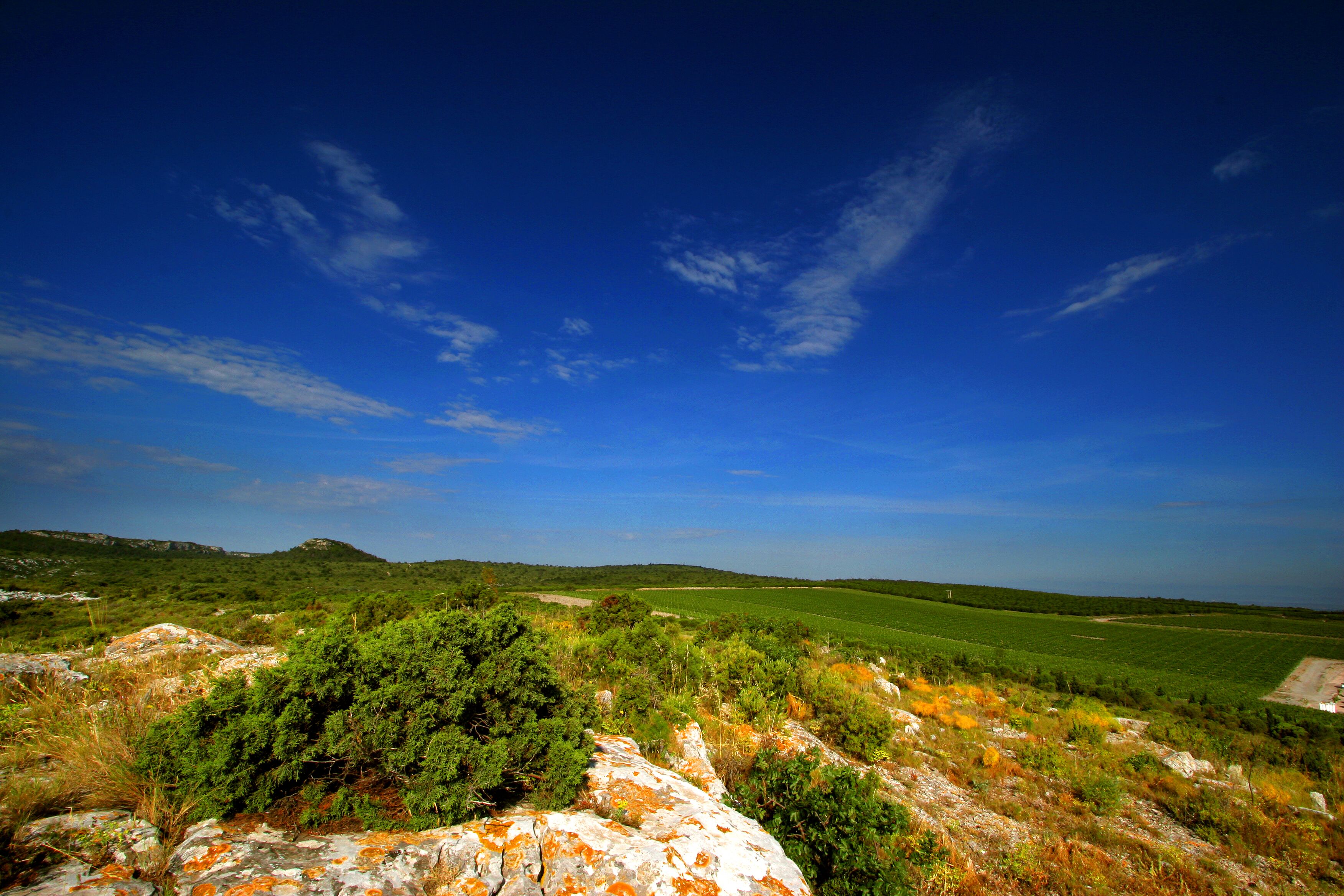 A landscape with a clear sky, green fields, and rocky terrain.
