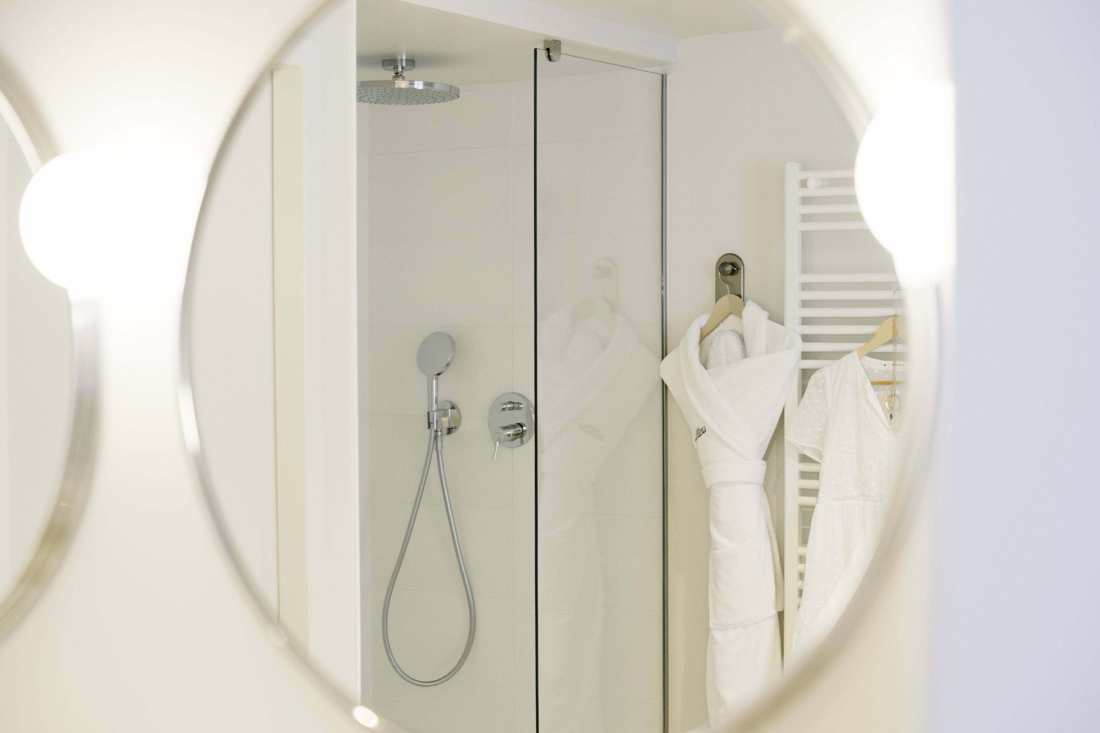 A modern bathroom with a glass shower enclosure, a handheld showerhead, and a white robe hanging on a rack.