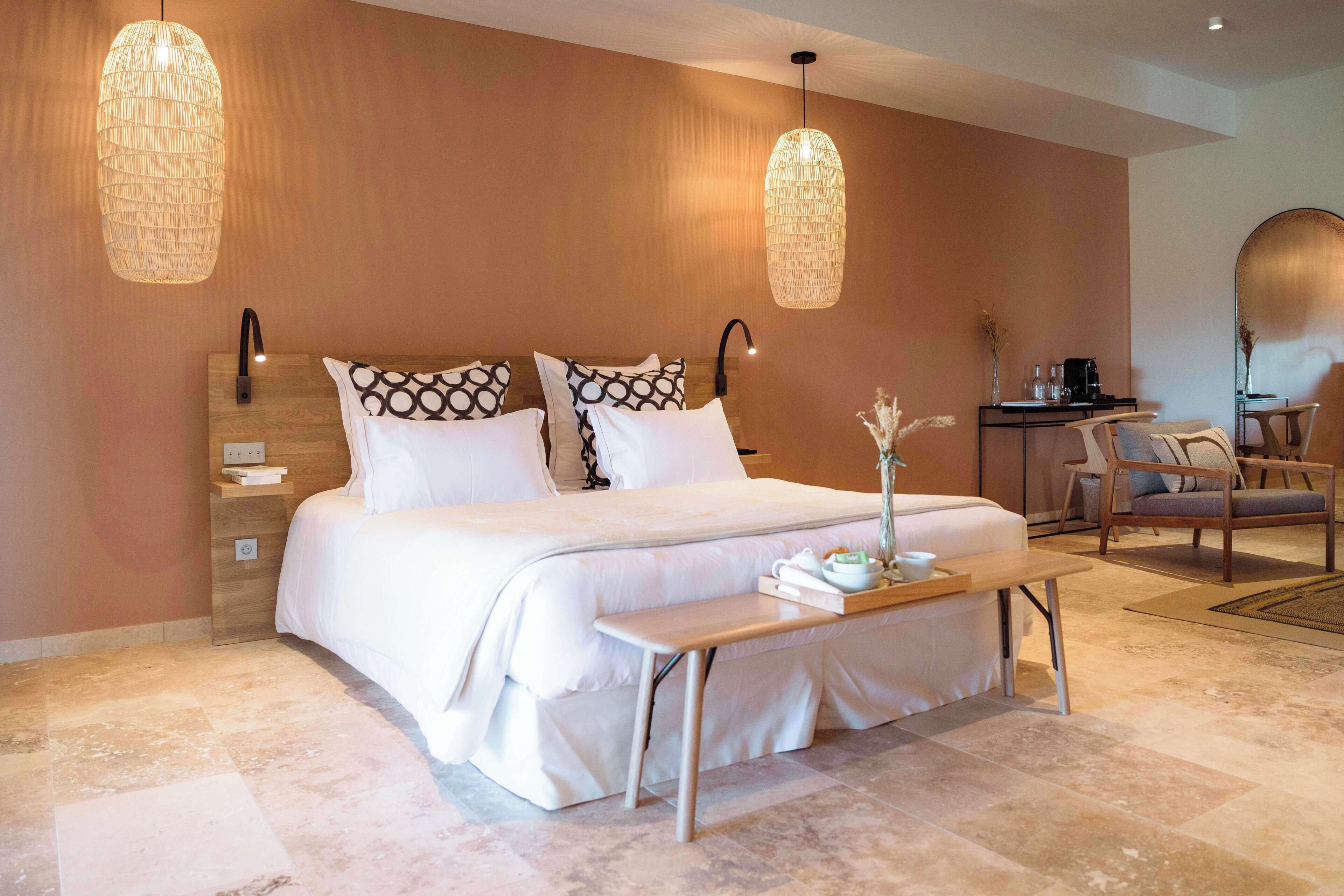 Een moderne slaapkamer met een groot bed, nachtkastjes, een bankje en twee hanglampen.