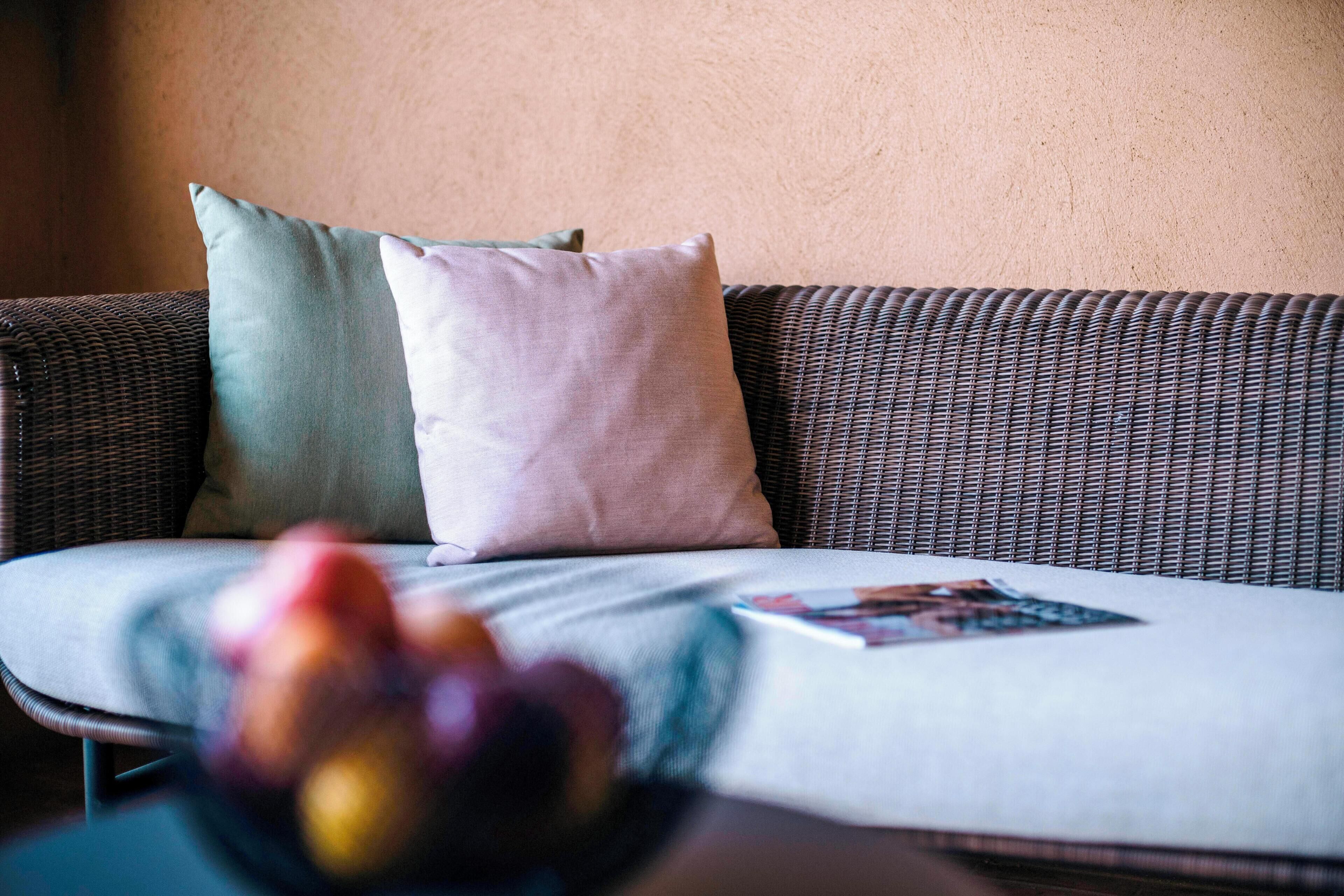 A wicker sofa with two pillows and a magazine on it.