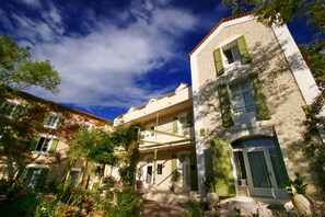 Ein traditionelles Gebäude mit Balkon, einer Treppe zum Eingang und einem Garten mit roten Blumen.