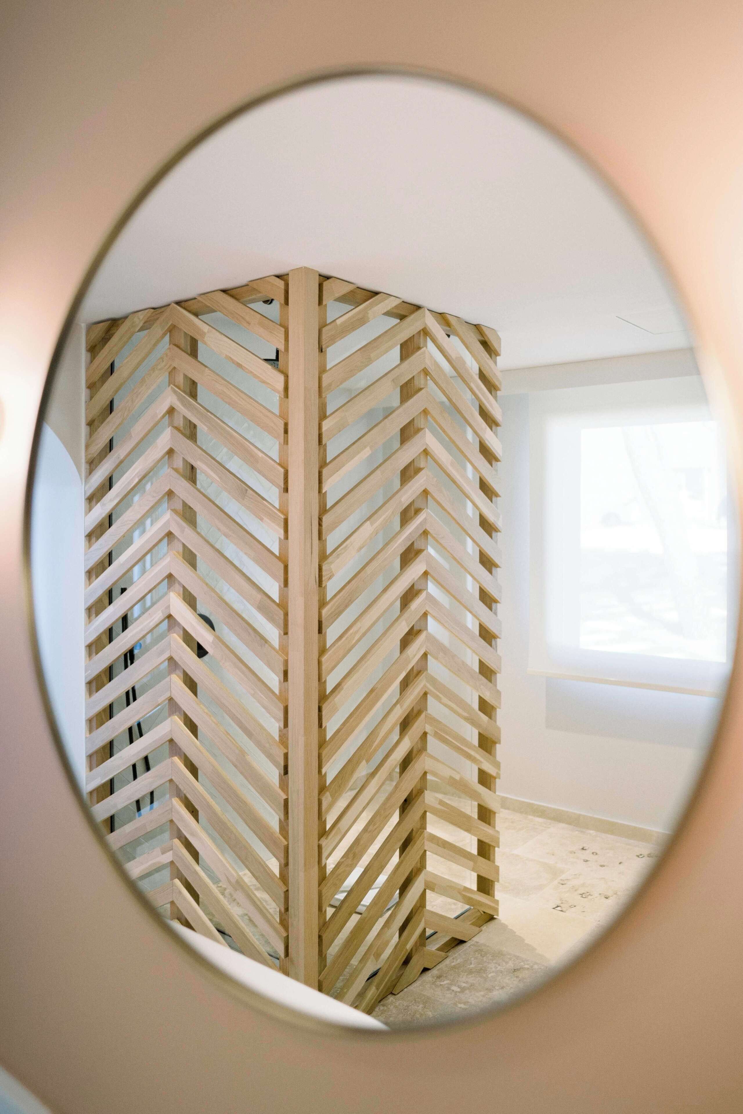 Une pièce dotée d’une cloison en bois à motifs en chevrons, d’une grande fenêtre et d’un miroir rond accroché au mur.