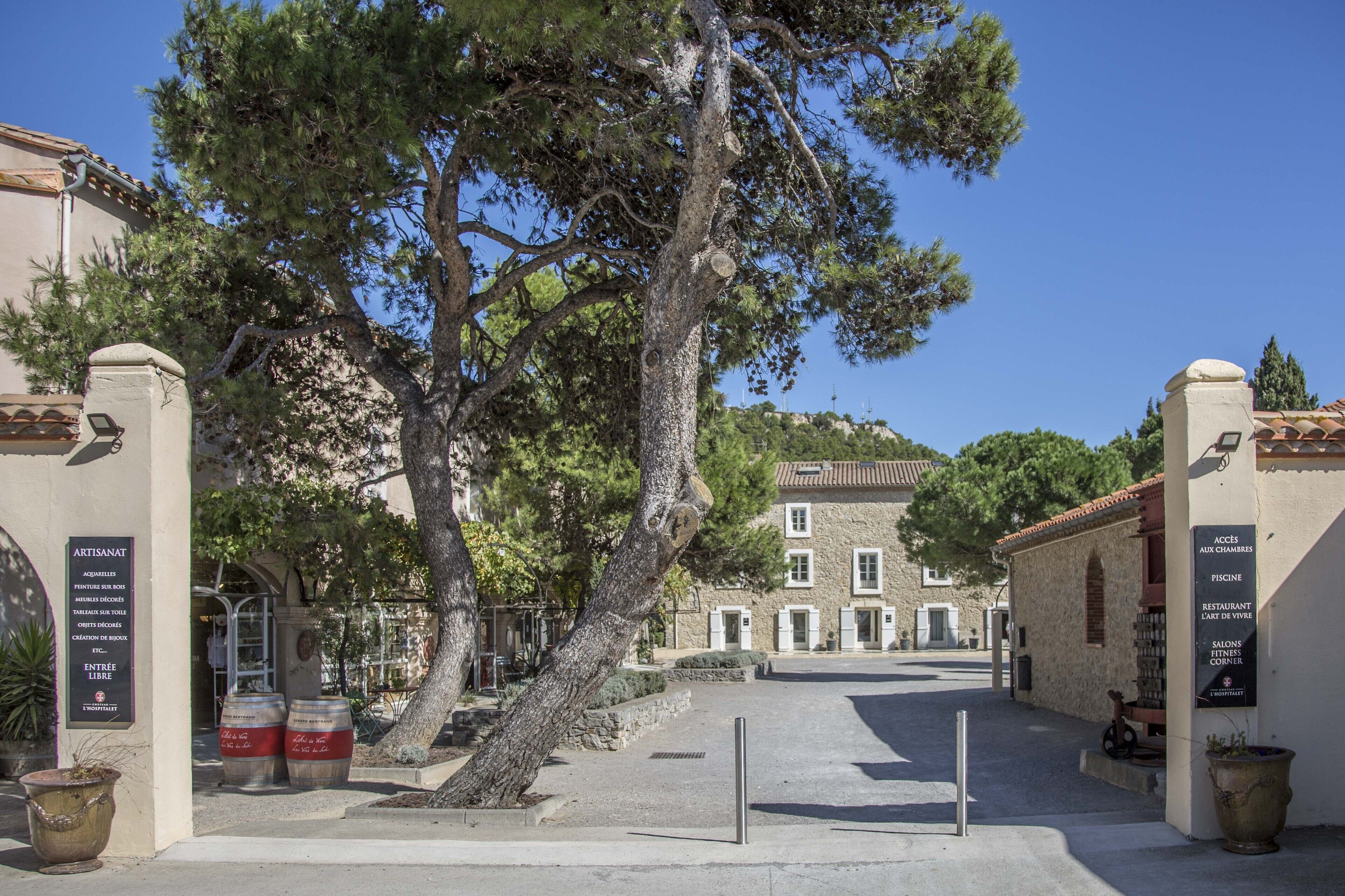 A courtyard with a large tree, stone buildings, and a sign indicating a restaurant and bar.