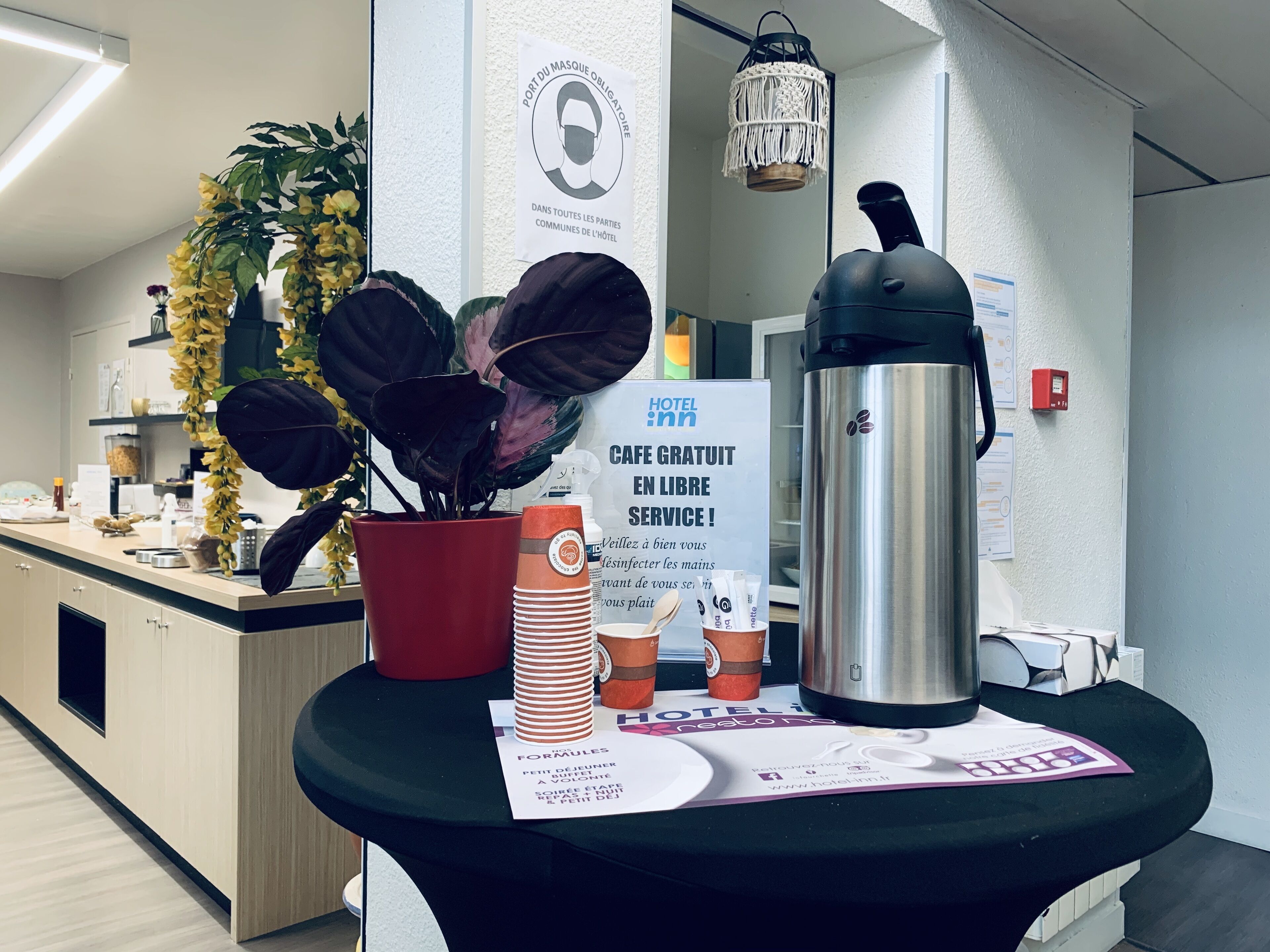 Un espace d’accueil d’hôtel comprenant un coin café, une plante en pot, un panneau indiquant que le Wi-Fi est gratuit et un extincteur.
