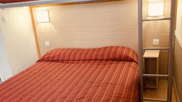 A bunk bed with a red striped bedspread, a wooden headboard, and a small wooden shelf.