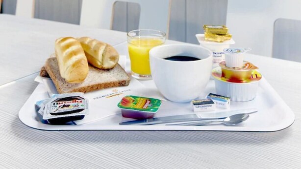 Uma bandeja de café da manhã com pão, suco, café e lanches sobre uma mesa de hotel.