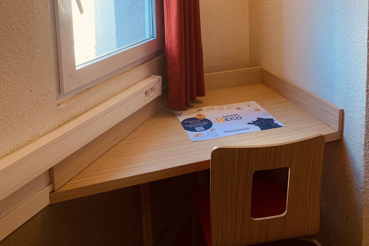 Habitación de esquina con ventana, cortina, escritorio con un mapa y una lámpara de pared.