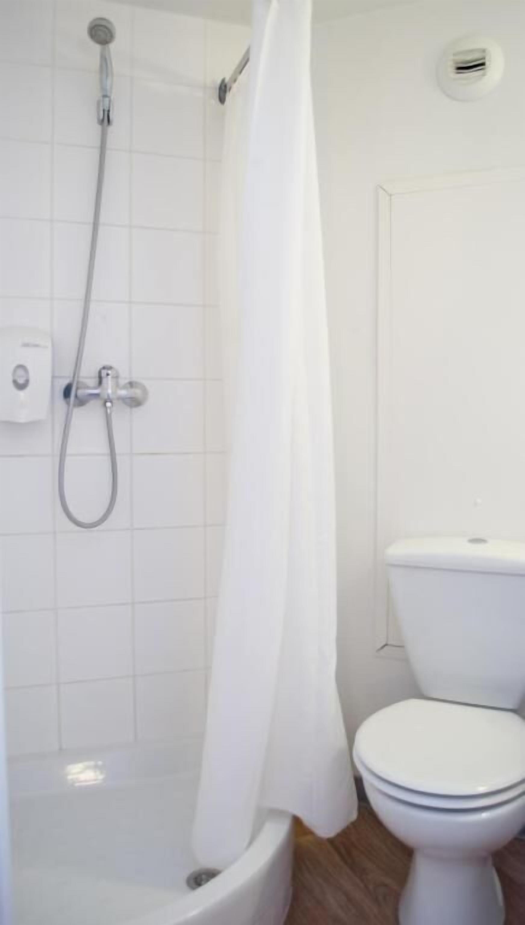 A bathroom with a shower, toilet, and a white tiled wall.