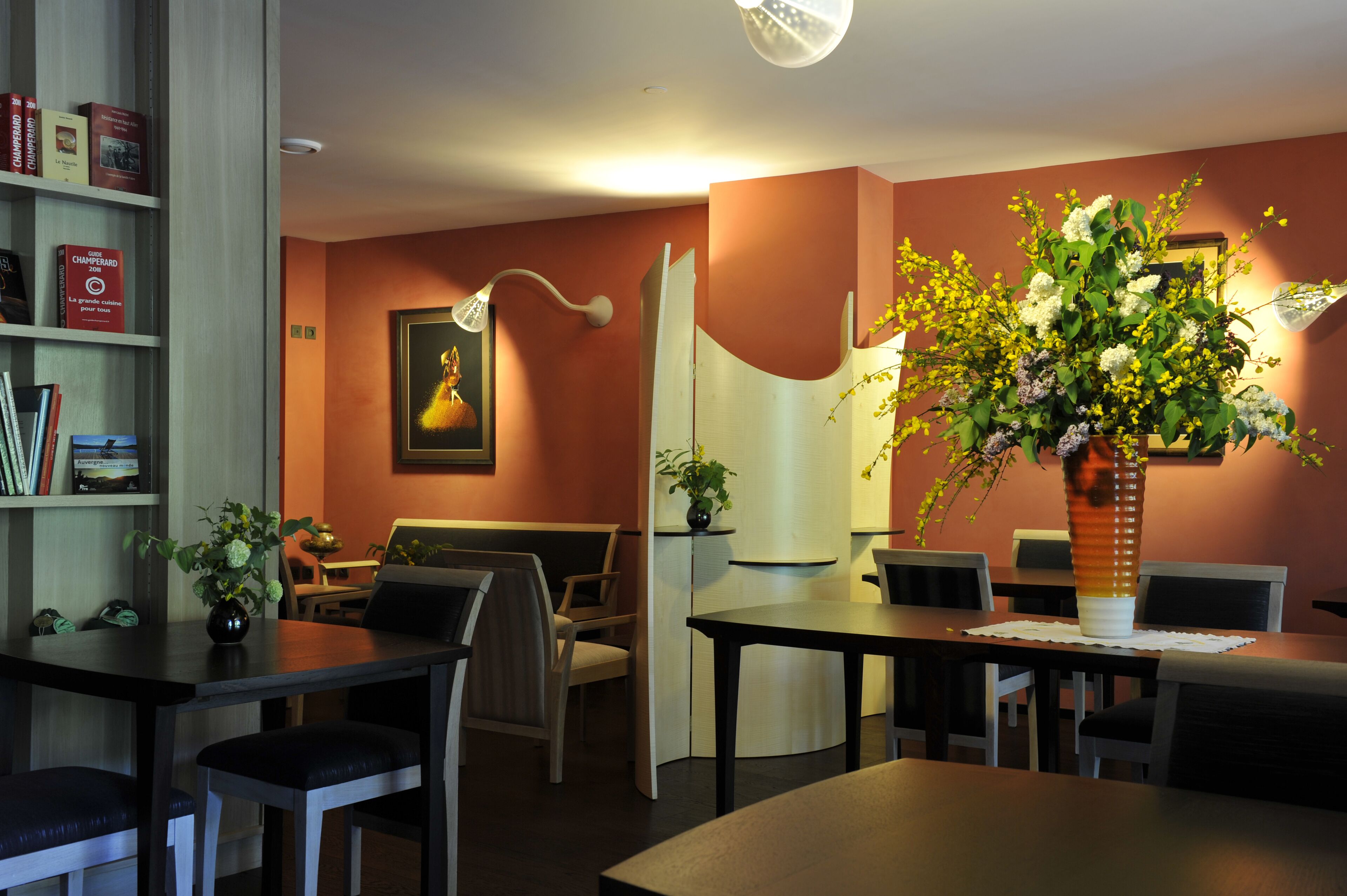 Un comedor con mesas y sillas, una estantería y un jarrón con flores.