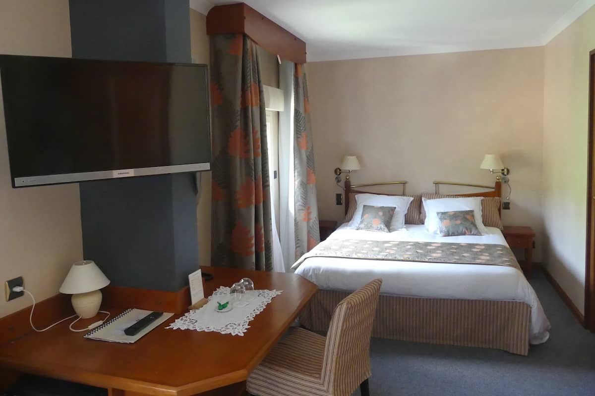 A hotel room with a single bed, a desk with a chair, a television, and a window with curtains.